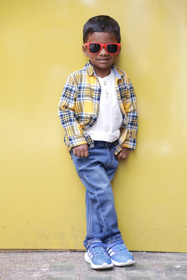 Murari in yellow plaid shirt and red sunglasses leaning against yellow wall